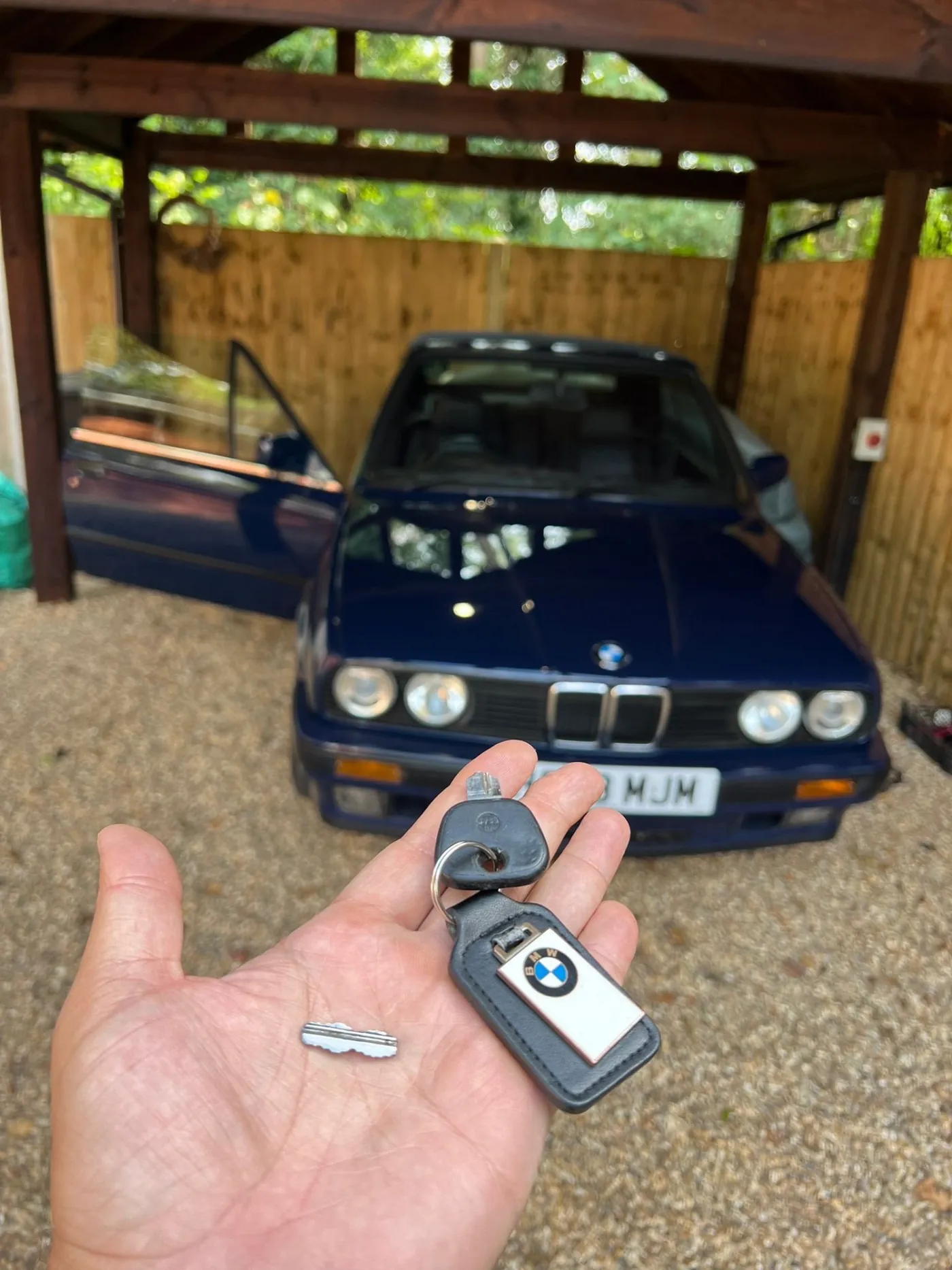 Broken BMW car key held in hand in front of a car